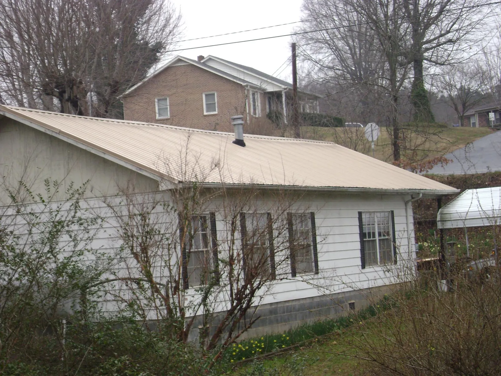 Tan metal roof on a white sided house set into a hillside — Commercial Roofing by Roofing Brothers in Davidsonville